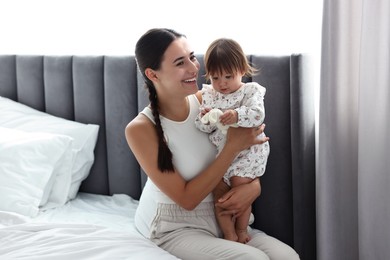 Beautiful young mother and her cute little baby with rabbit toy on bed at home