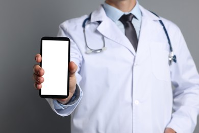 Photo of Doctor showing smartphone with blank screen on grey background, closeup. Mockup for design