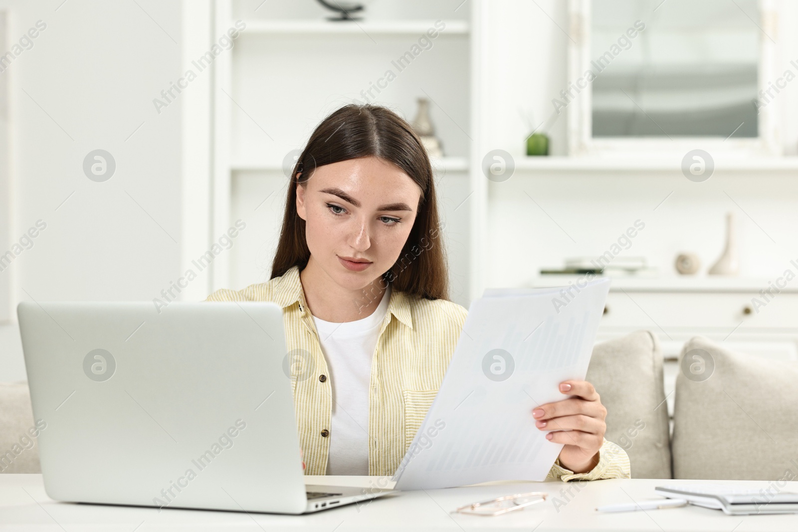 Photo of Budget planning. Young woman with papers using laptop at white table indoors