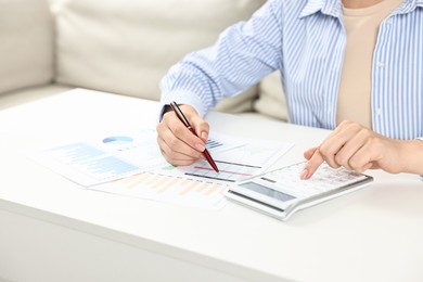 Photo of Budget planning. Woman with papers using calculator at white table, closeup