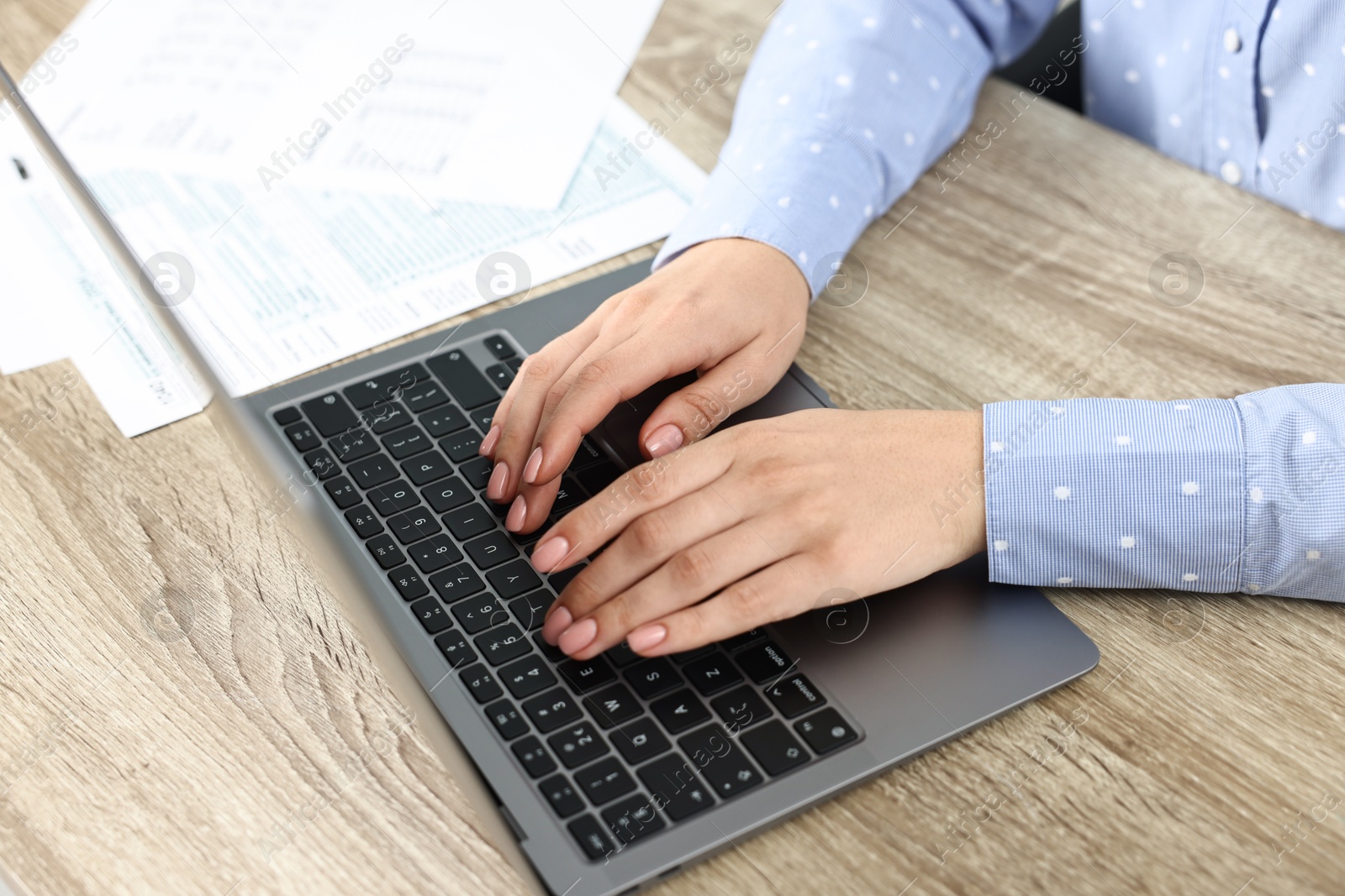 Photo of Budget planning. Woman with papers using laptop at wooden table, closeup