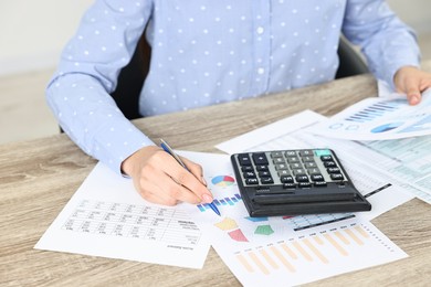 Budget planning. Woman with papers and calculator at wooden table, closeup