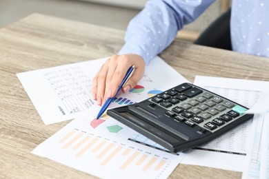 Photo of Budget planning. Woman with papers and calculator at wooden table, closeup