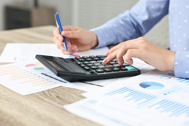 Photo of Budget planning. Woman with papers using calculator at wooden table, closeup