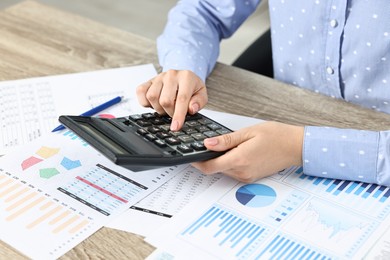 Photo of Budget planning. Woman with papers using calculator at wooden table, closeup