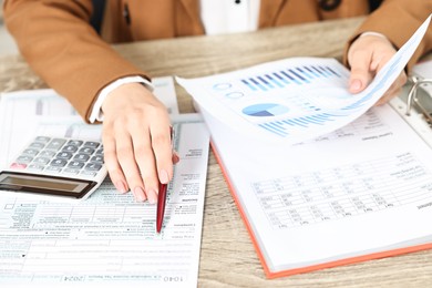 Budget planning. Woman with papers and calculator at wooden table, closeup