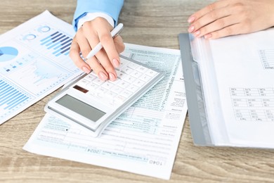 Budget planning. Woman with papers and calculator at wooden table, closeup