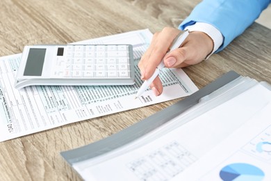 Photo of Budget planning. Woman with papers and calculator at wooden table, closeup