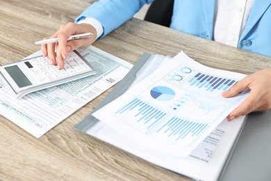 Photo of Budget planning. Woman with papers and calculator at wooden table, closeup