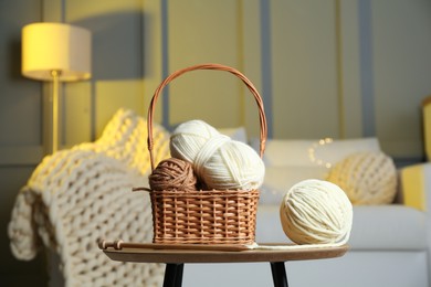 Photo of Wicker basket with colorful yarns and knitting needles on coffee table in cozy room