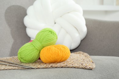 Photo of Skeins of soft yarn and knitting needles on sofa indoors