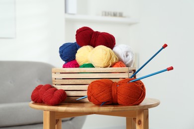 Photo of Skeins of soft yarn in crate and knitting needles on wooden table indoors