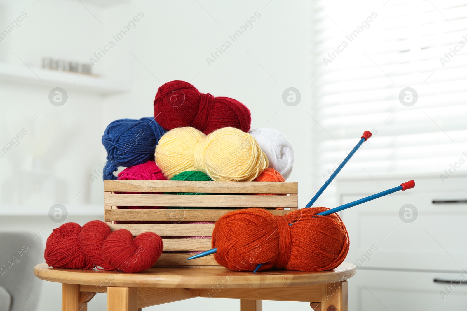 Photo of Skeins of soft yarn in crate and knitting needles on wooden table indoors