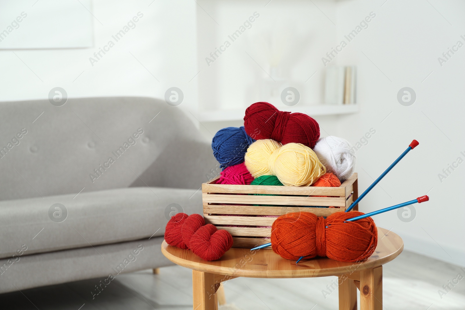 Photo of Skeins of soft yarn in crate and knitting needles on wooden table indoors