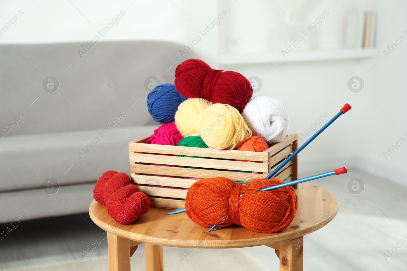 Photo of Skeins of soft yarn in crate and knitting needles on wooden table indoors