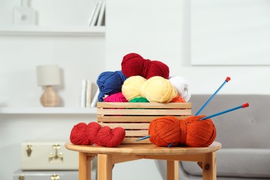 Photo of Skeins of soft yarn in crate and knitting needles on wooden table indoors