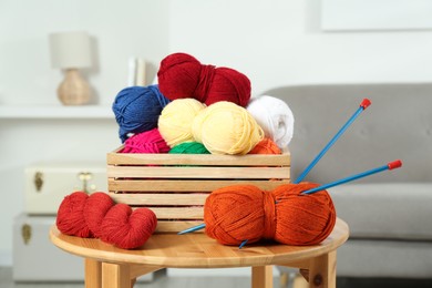 Photo of Skeins of soft yarn in crate and knitting needles on wooden table indoors