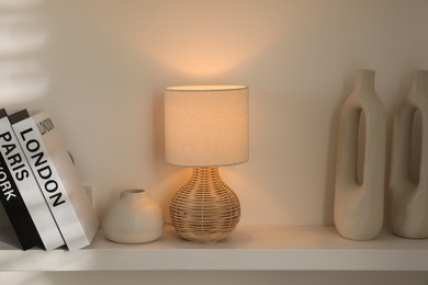 Photo of Lamp, ceramic vases and books on white shelf