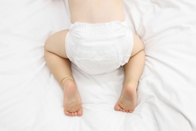 Photo of Little child in diaper on bed at home, closeup