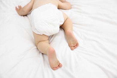 Photo of Little child in diaper on bed at home, closeup