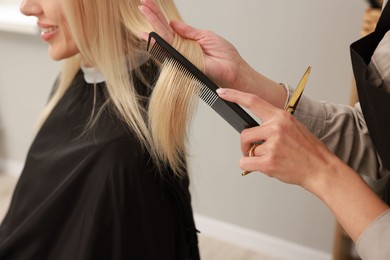 Professional hairdresser combing woman's hair in salon, closeup