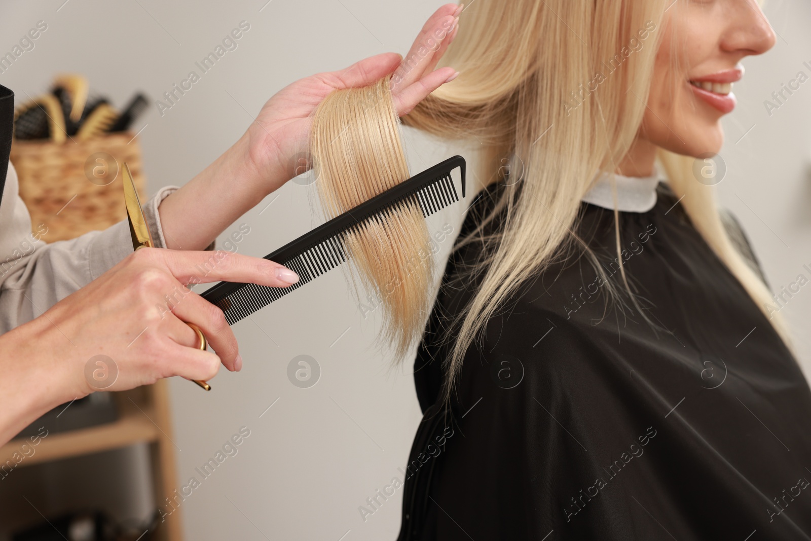 Photo of Professional hairdresser combing woman's hair in salon, closeup