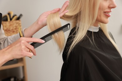 Photo of Professional hairdresser combing woman's hair in salon, closeup