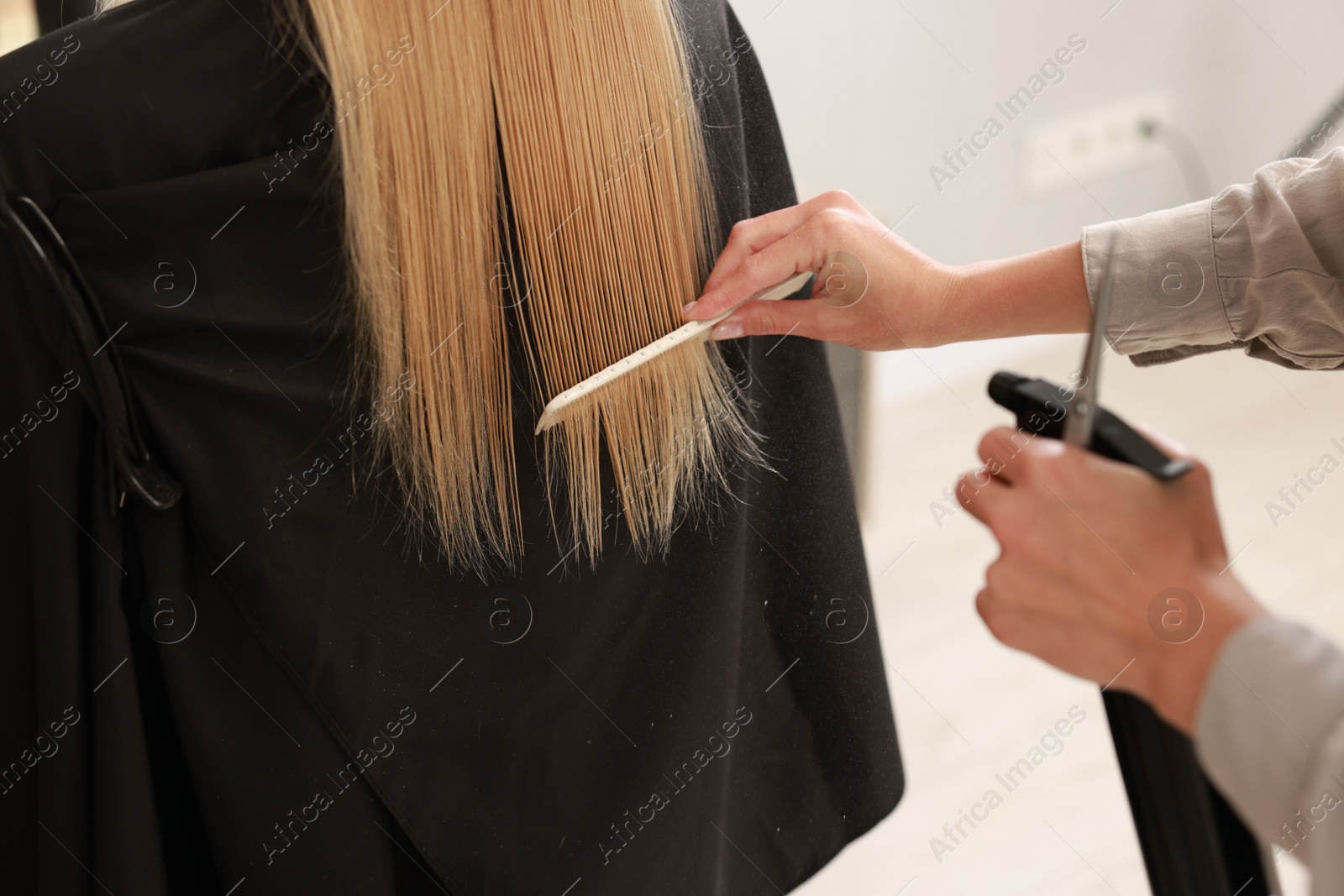 Photo of Hairdresser using spray while making stylish haircut in salon, closeup