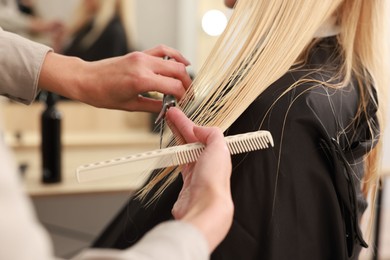 Photo of Hairdresser cutting client's hair with scissors in salon, closeup