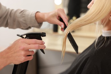 Hairdresser using spray while making stylish haircut in salon, closeup