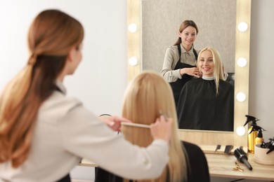 Photo of Professional hairdresser combing woman's hair in salon, selective focus