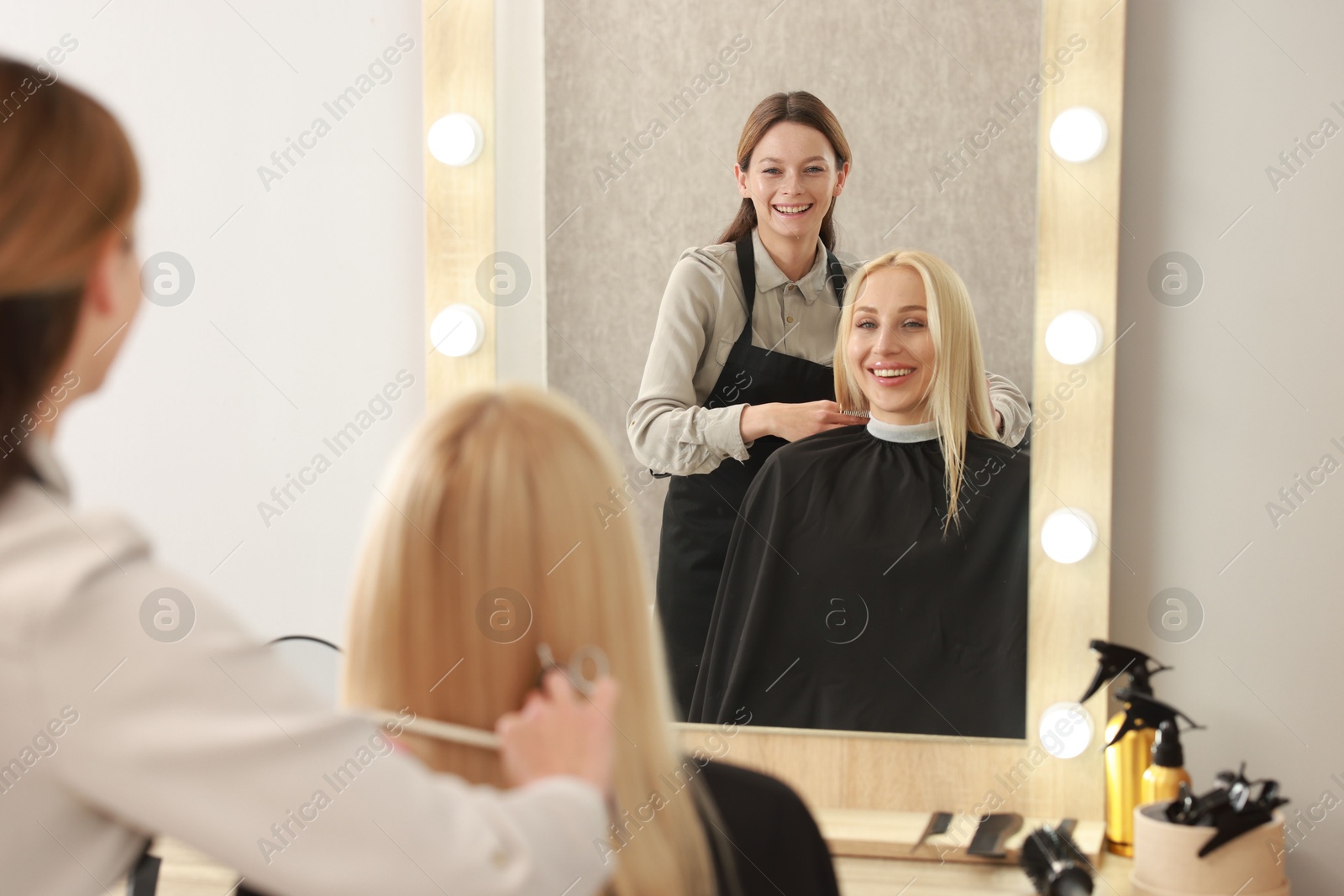 Photo of Professional hairdresser combing woman's hair in salon, selective focus