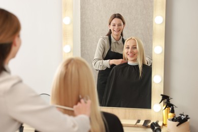 Photo of Professional hairdresser combing woman's hair in salon, selective focus