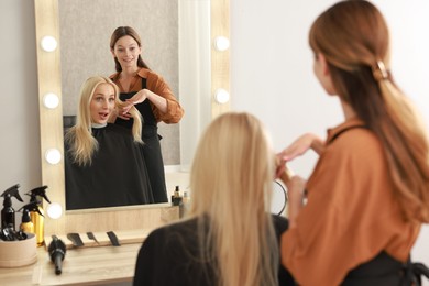 Hairdresser cutting client's hair with scissors in salon, selective focus