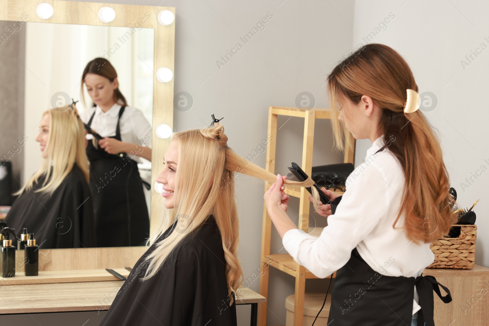 Photo of Hairdresser curling woman's hair with flat iron in salon