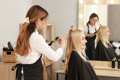 Photo of Hairdresser curling woman's hair with flat iron in salon