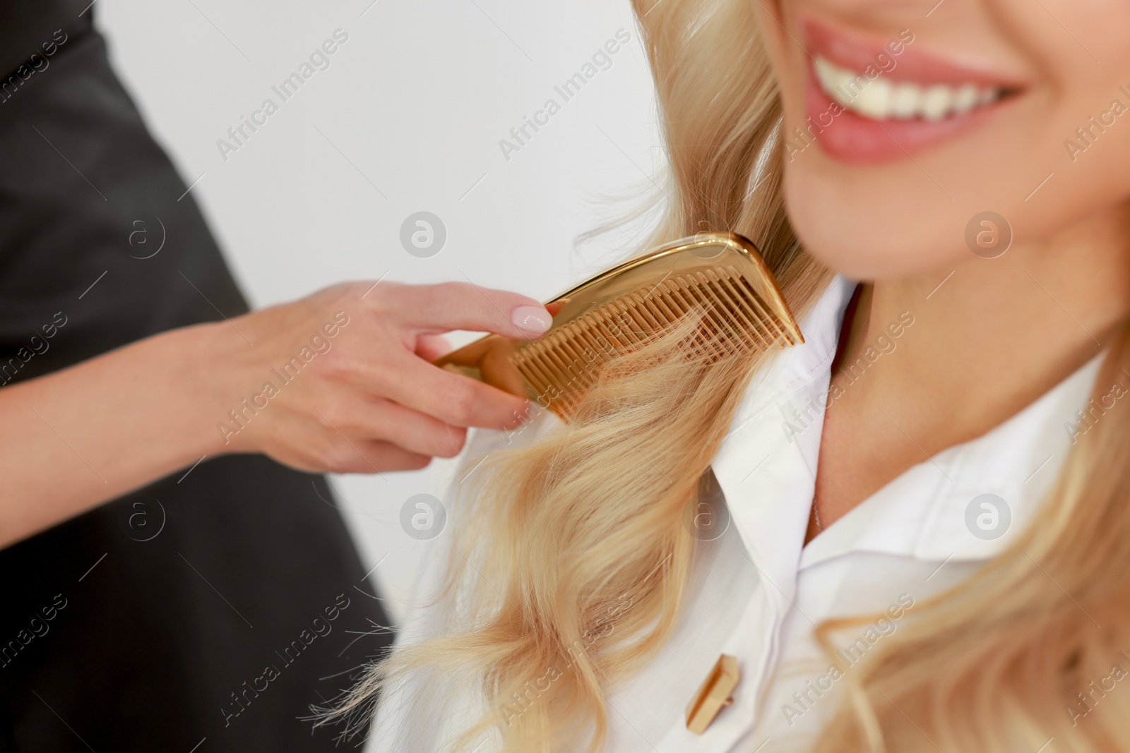 Photo of Professional hairdresser combing woman's hair in salon, closeup