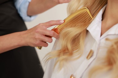 Photo of Professional hairdresser combing woman's hair in salon, closeup