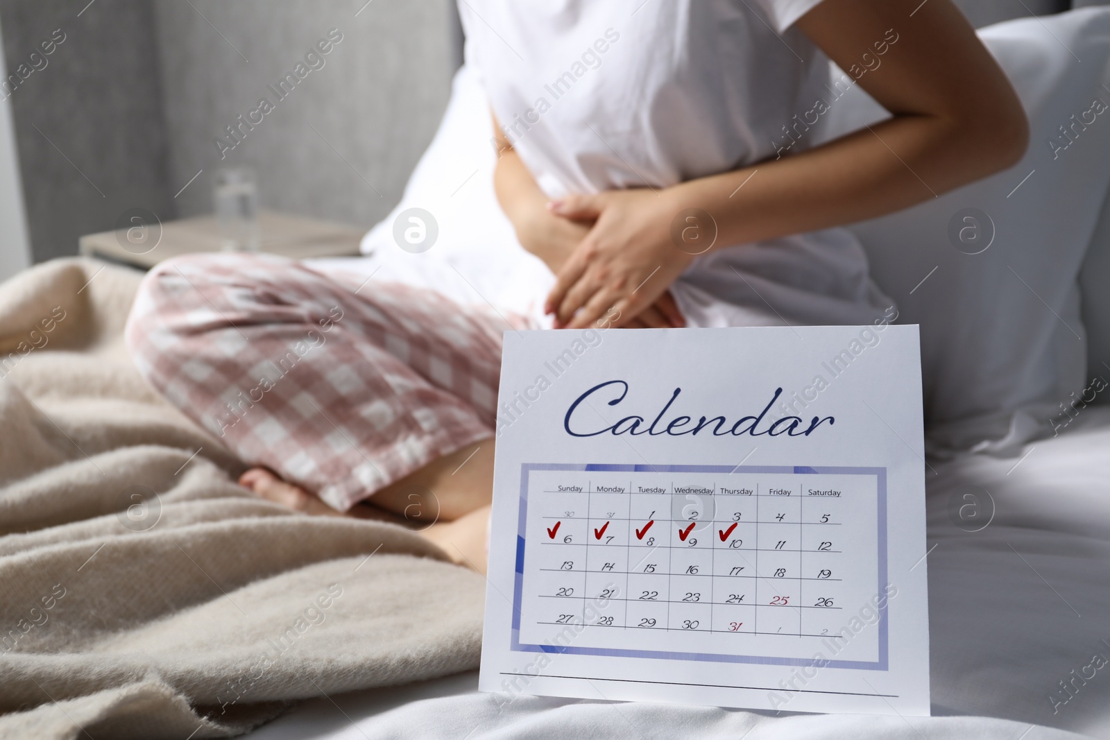 Photo of Woman suffering from abdominal pain in bed at home, focus on calendar with marked menstrual cycle days