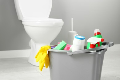 Photo of Bucket with different toilet cleaners, rag, sponge and gloves in bathroom