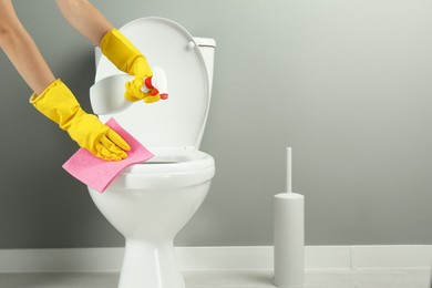 Photo of Woman with spray and rag cleaning toilet seat in bathroom, closeup