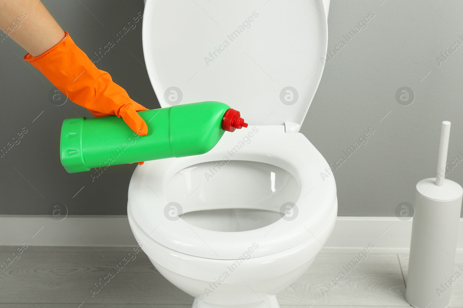 Photo of Woman cleaning toilet with detergent in bathroom, closeup