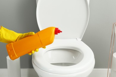 Photo of Woman cleaning toilet with detergent in bathroom, closeup