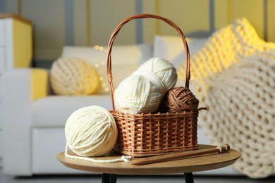 Photo of Wicker basket with colorful yarns and knitting needles on coffee table in cozy room