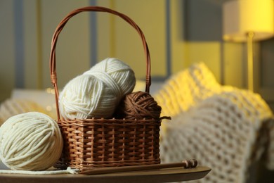 Photo of Wicker basket with colorful yarns and knitting needles on coffee table in cozy room