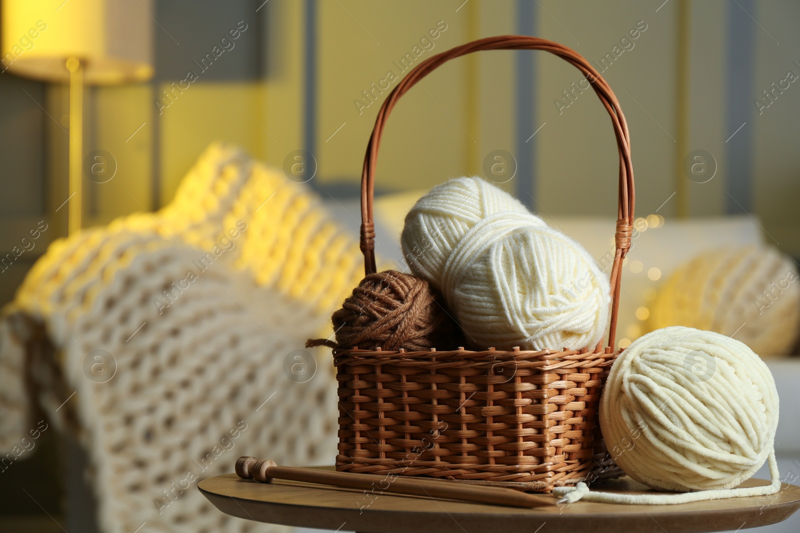 Photo of Wicker basket with colorful yarns and knitting needles on coffee table in cozy room