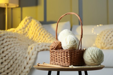 Photo of Wicker basket with colorful yarns and knitting needles on coffee table in cozy room