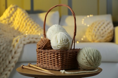 Photo of Wicker basket with colorful yarns and knitting needles on coffee table in cozy room