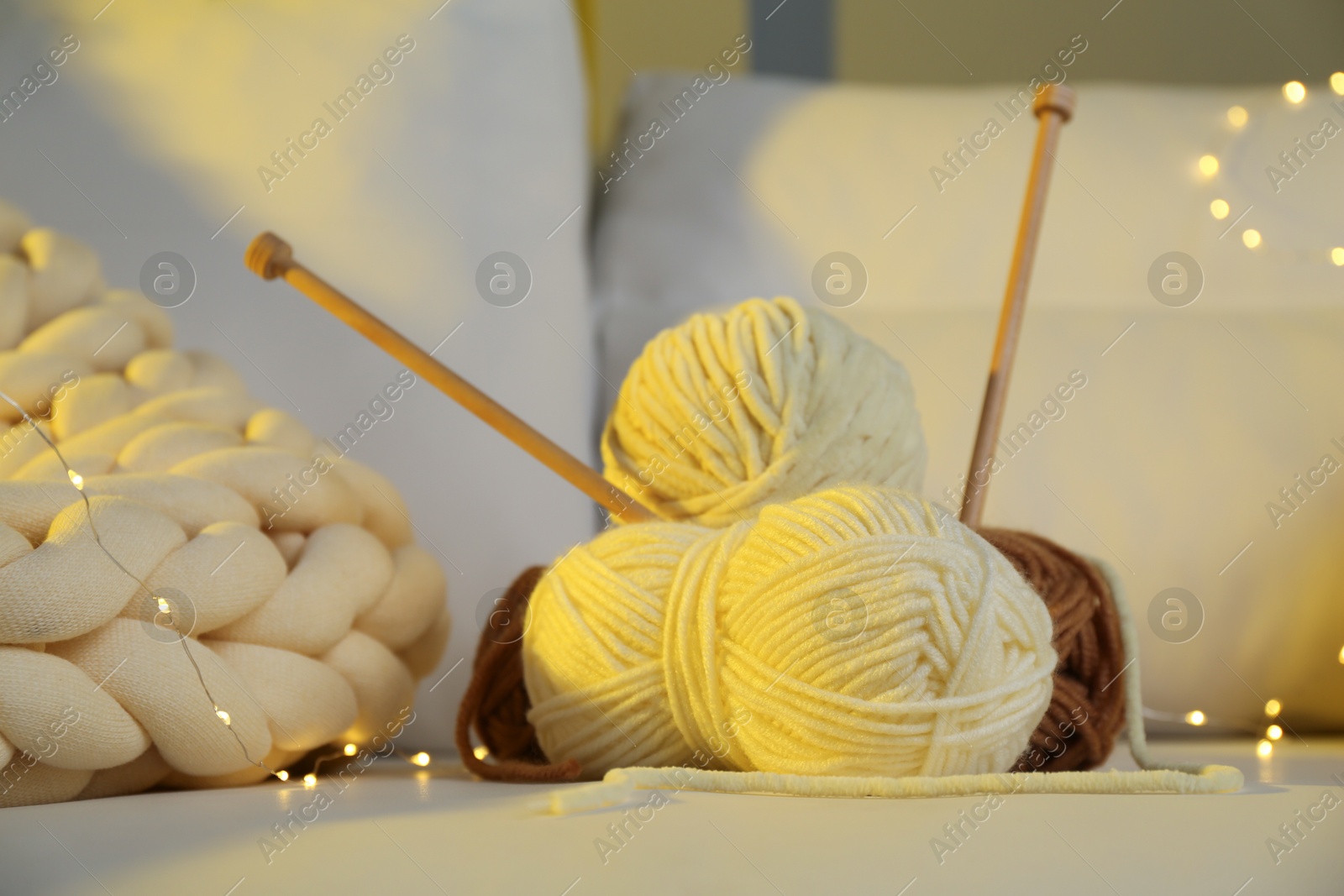 Photo of Skeins of yarn, knitting needles and festive lights on sofa