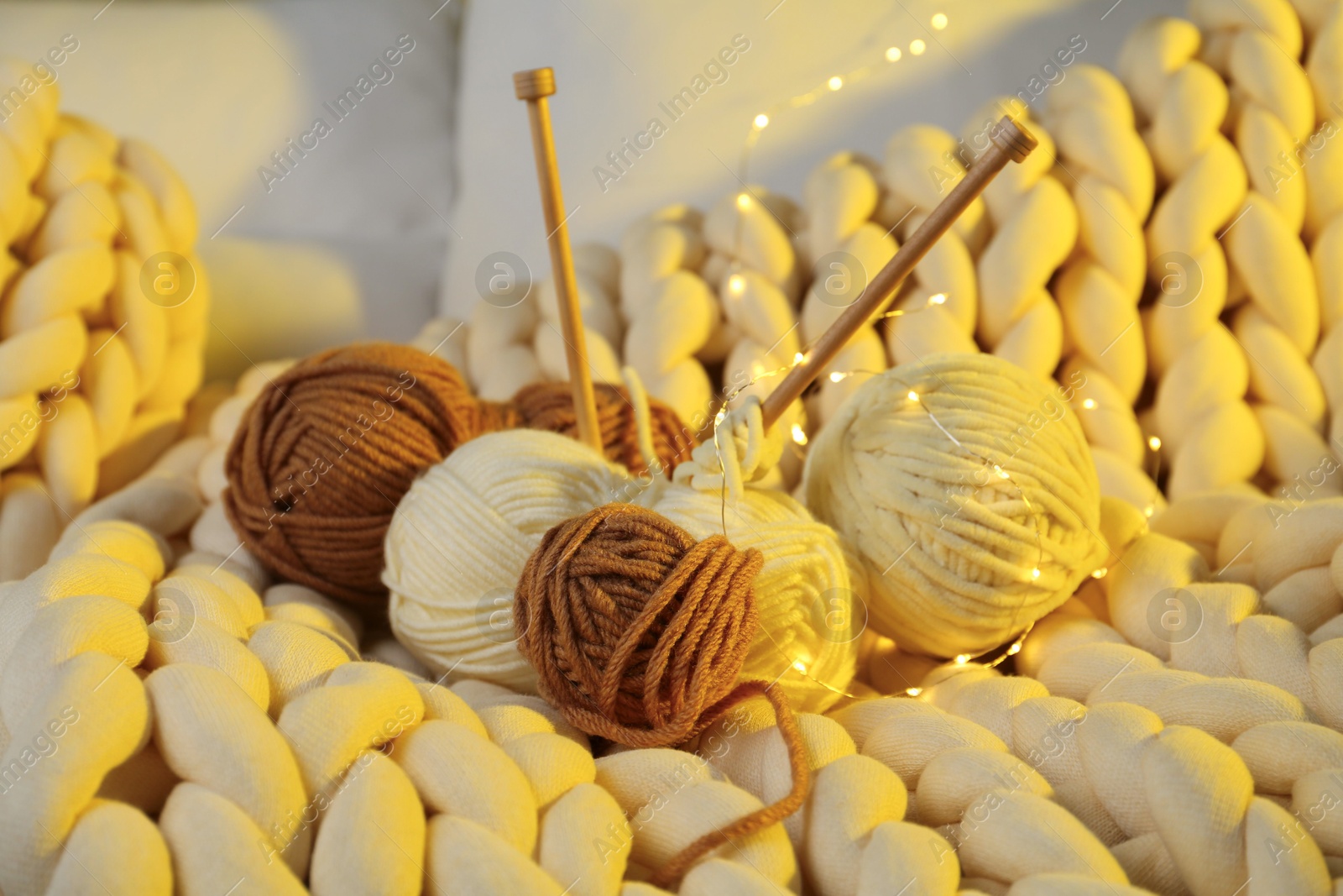 Photo of Colorful yarns, knitting needles and festive lights on blanket